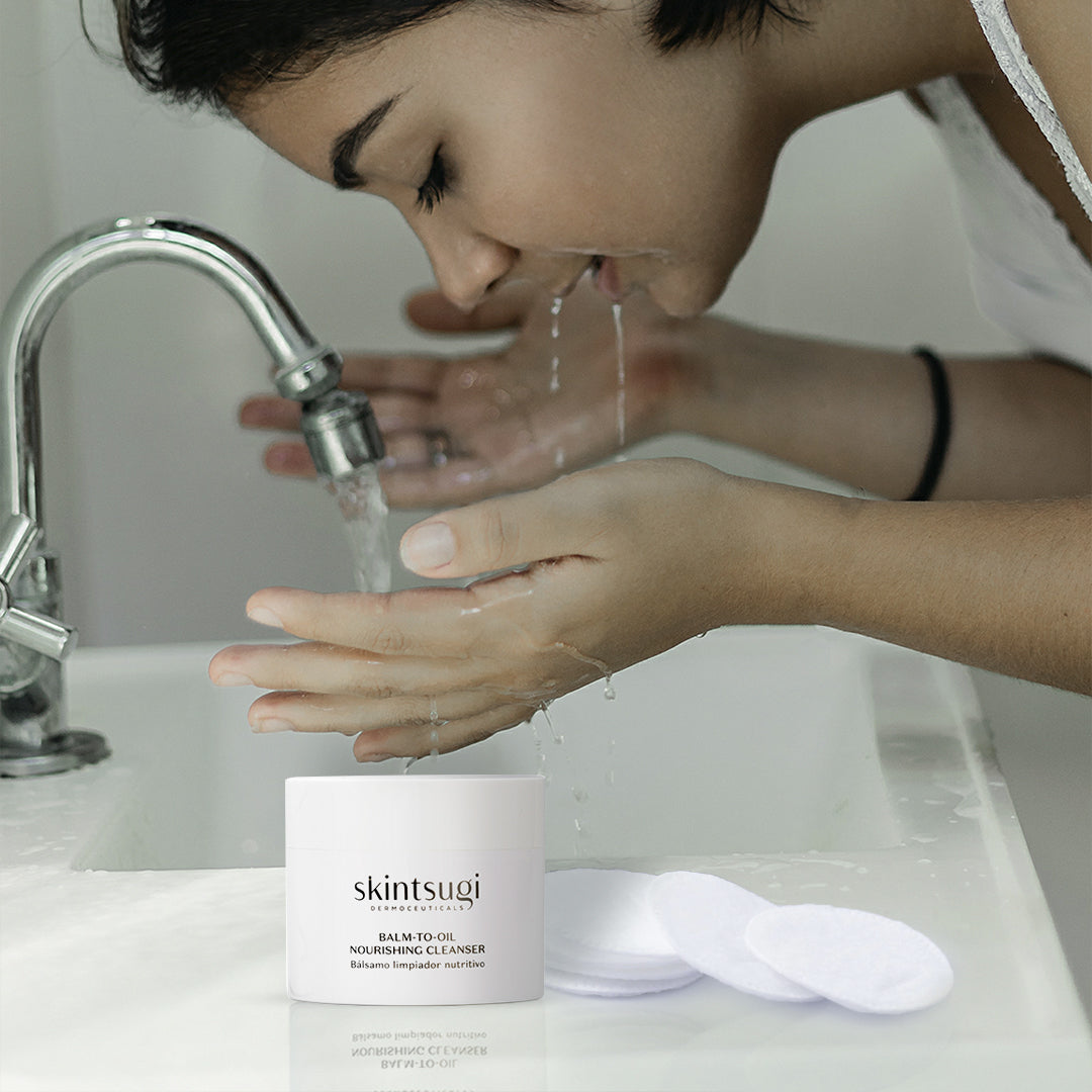Dunkelhaariges Modell wäscht sich im Waschbecken das Gesicht mit Reichhaltige Reinigungsbalsam ab